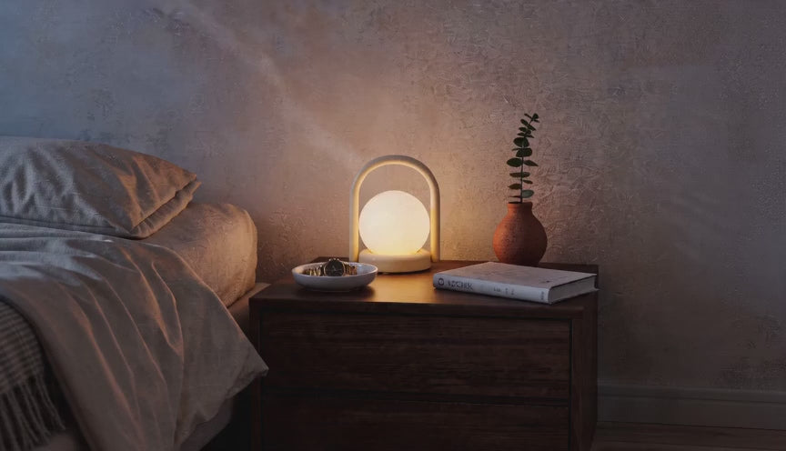 Cinematic video of a cordless LED globe lantern lamp glowing softly on a wooden bedside table in a dim bedroom.