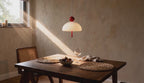 Cinematic video of a white opal glass dome pendant lamp with red ball cap and pull cord hanging above a sunlit dining table.