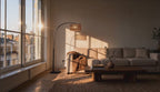 Cinematic video of an arc floor lamp with woven rattan drum shade arching over a sunlit living room at golden hour.