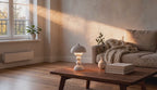 Cinematic video of a white mushroom dome table lamp glowing softly on a wooden coffee table beside a linen sofa in sunlit living room.