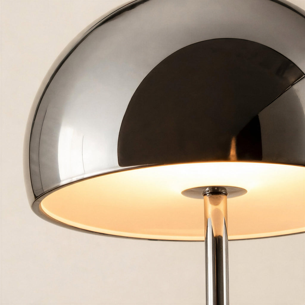 Close-up of the chrome dome shade reflecting soft light, warm bulb glow visible underneath above the slender mirrored stem