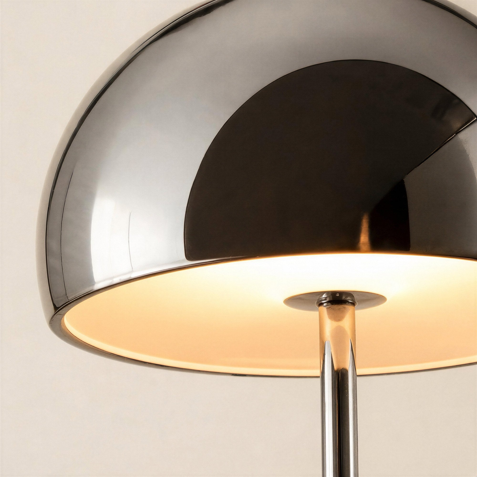 Close-up of the chrome dome shade reflecting soft light, warm bulb glow visible underneath above the slender mirrored stem