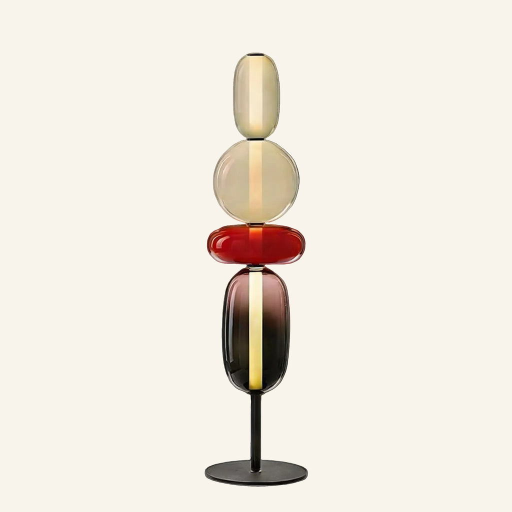 Stacked glass pebble floor lamp with amber, cherry red and smoke tinted shades on a black disc base, studio shot on cream background