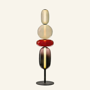 Stacked glass pebble floor lamp with amber, cherry red and smoke tinted shades on a black disc base, studio shot on cream background