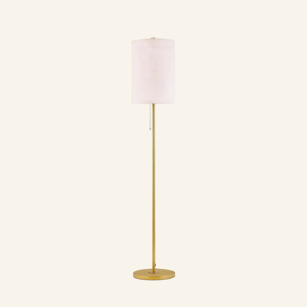 Slim floor lamp with cream linen drum shade on a slender brass-finished steel pole, round base, and pull-chain switch shown on cream backdrop.