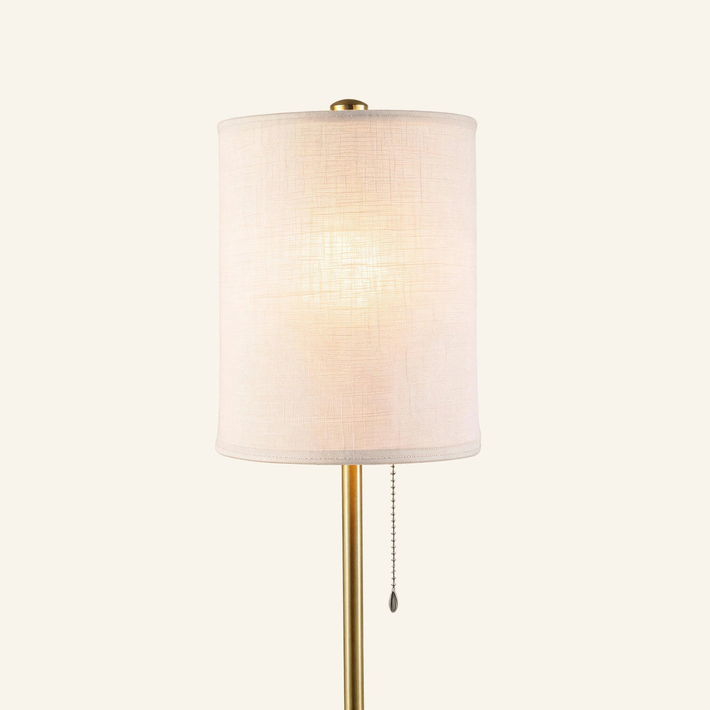 Close-up of the cylindrical linen drum shade glowing softly, revealing woven texture, brass cap, and beaded pull chain on the polished pole.