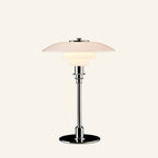 Three-tiered opal glass table lamp with polished chrome stem and round base, shown on cream studio background for bedside use.