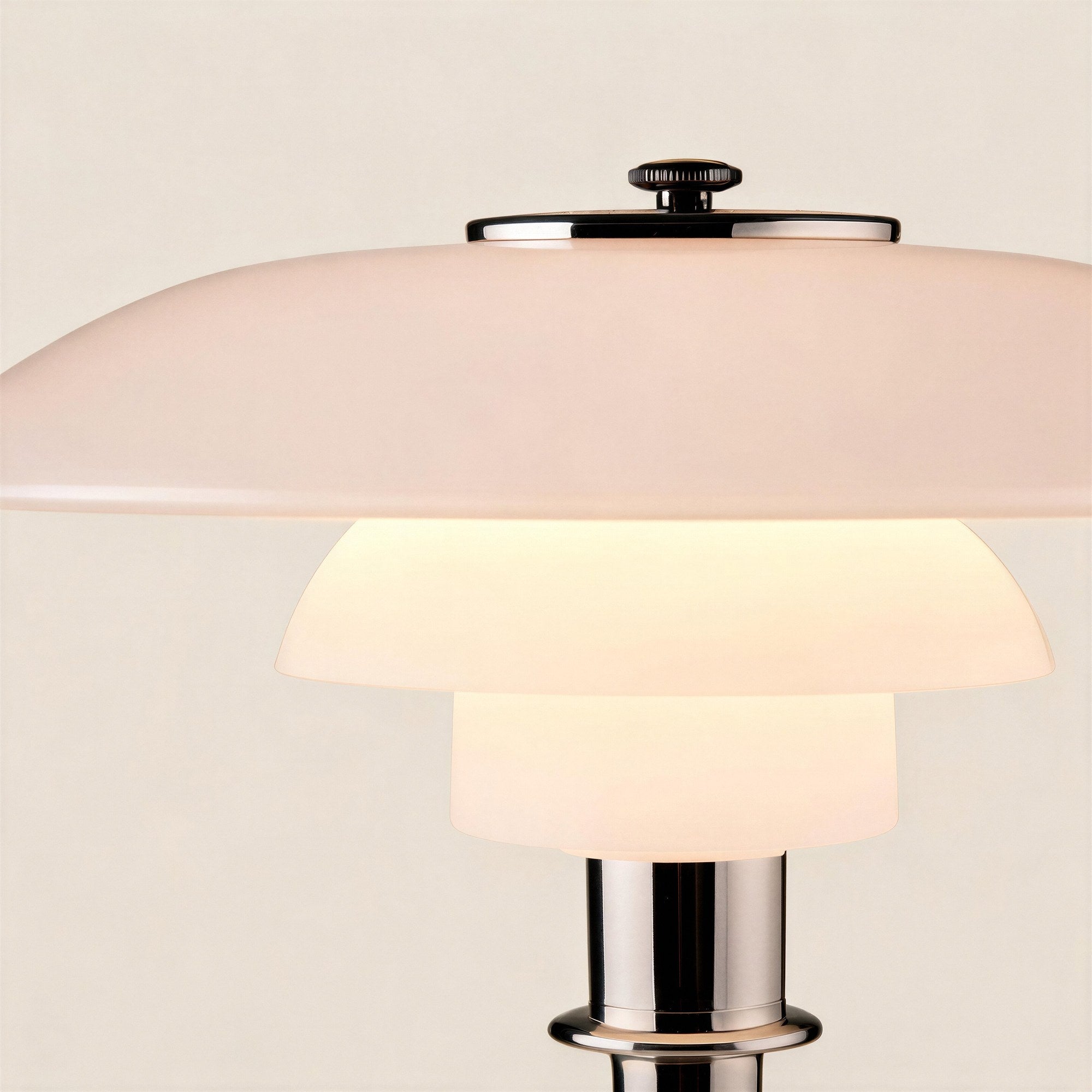 Close-up of stacked frosted glass shades glowing warm white, with chrome finial and polished metal column visible below.
