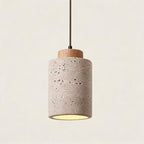 Studio shot of a mini cylinder pendant pairing pale travertine with a light oak collar, soft amber light spilling from the open base.