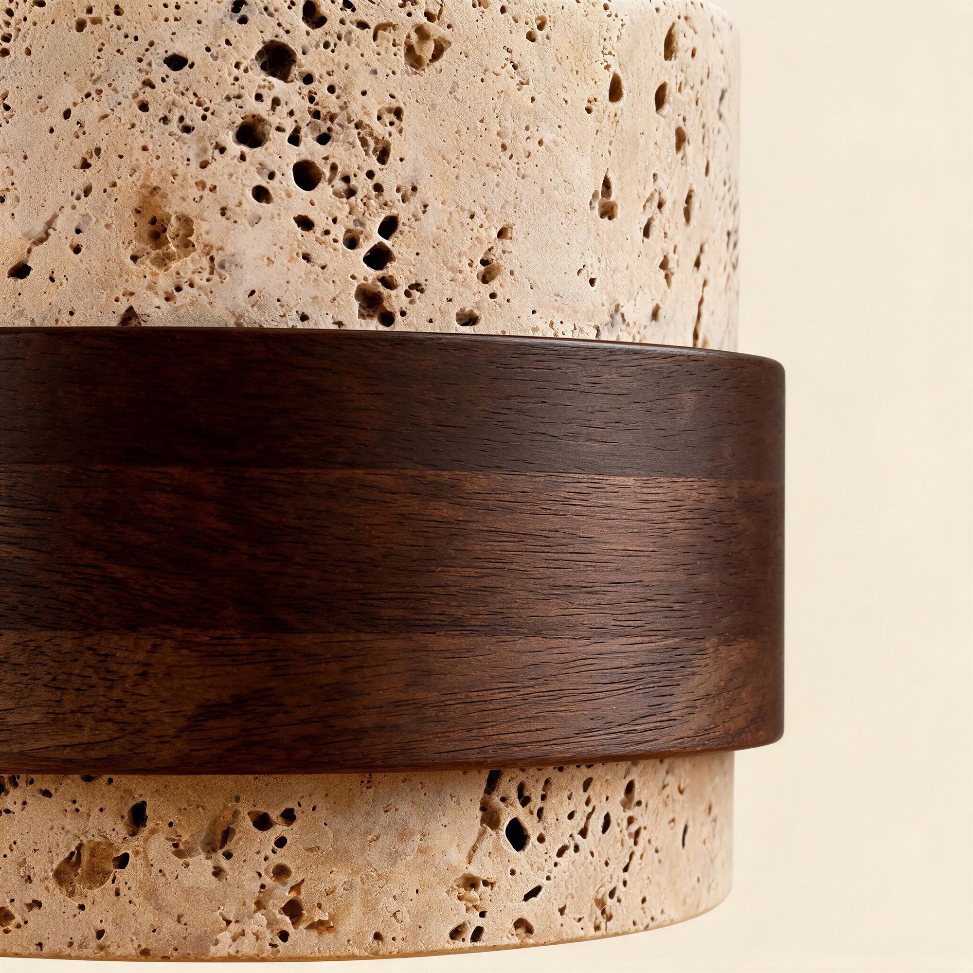 Close-up of porous travertine stone shade meeting a smooth walnut veneer band, highlighting natural pitting and warm grain detail.