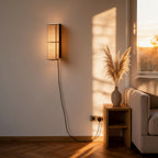 Cylindrical linen wall sconce mounted by a sofa in a sunset-lit living room with pampas grass nearby.